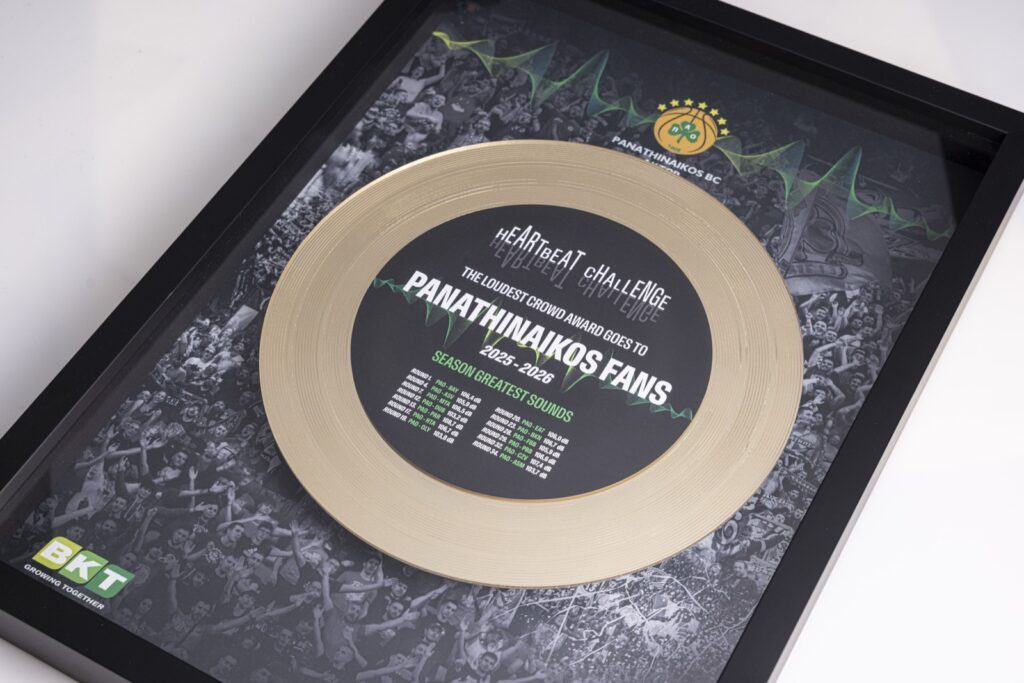 Il premio BKT Heartbeat Challenge visto di lato: il disco oro rialzato dal fondo sembra sospeso sopra la curva del Panathinaikos, in una cornice nera profonda